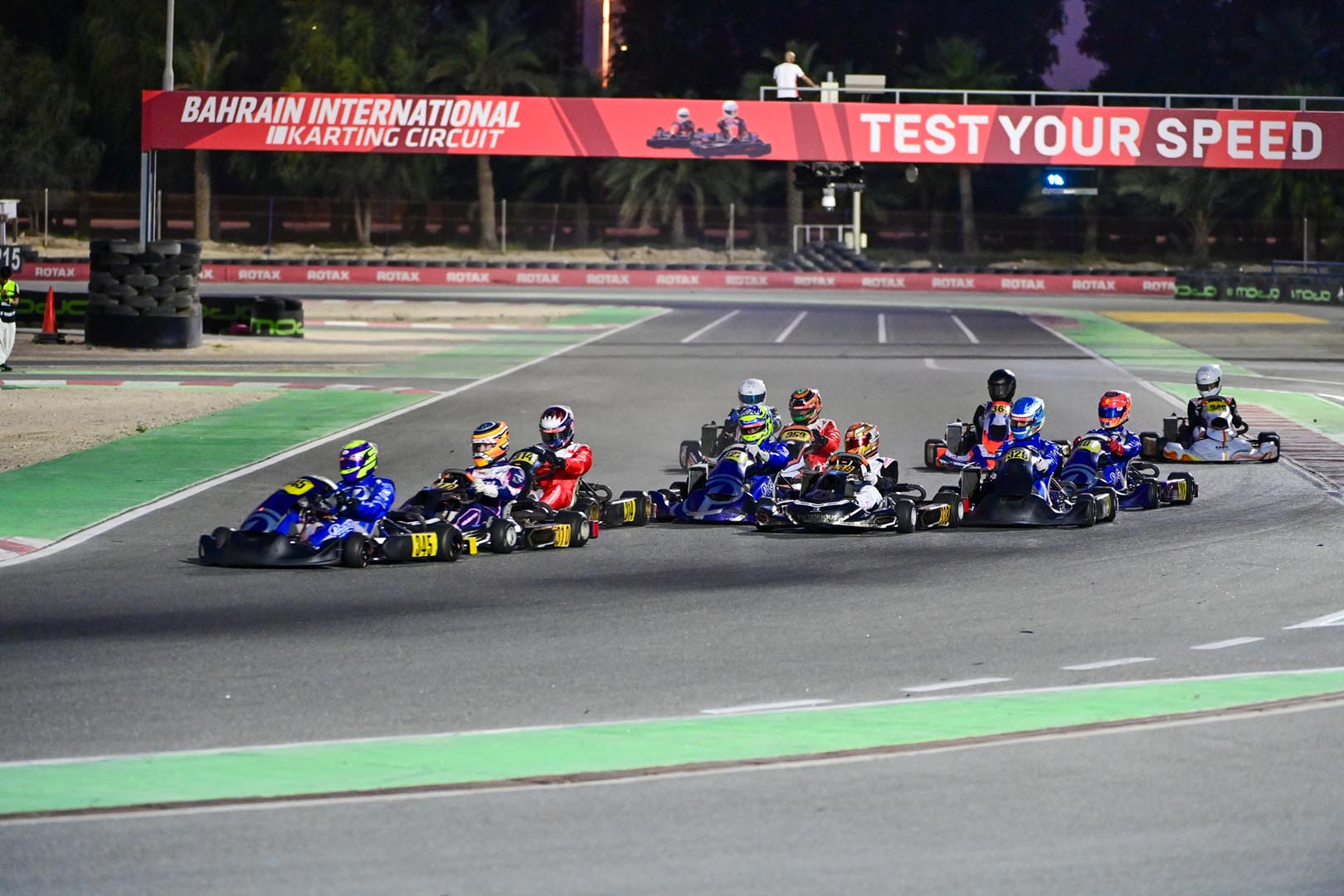 A field of helmeted kart drivers at Bahrain International Karting Circuit