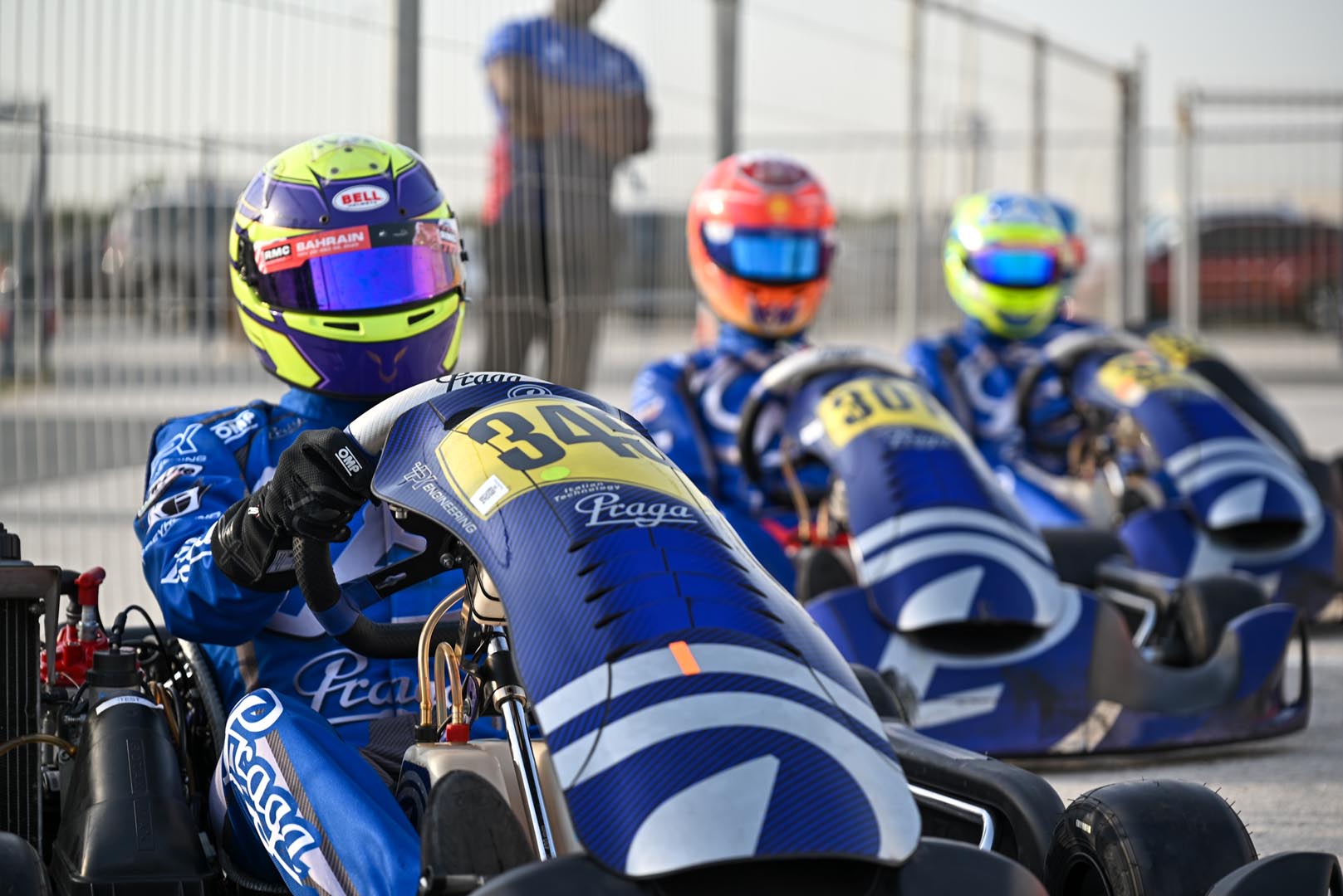 Kart drivers preparing on the Bahrain grid with faces obscured by mirrored visors