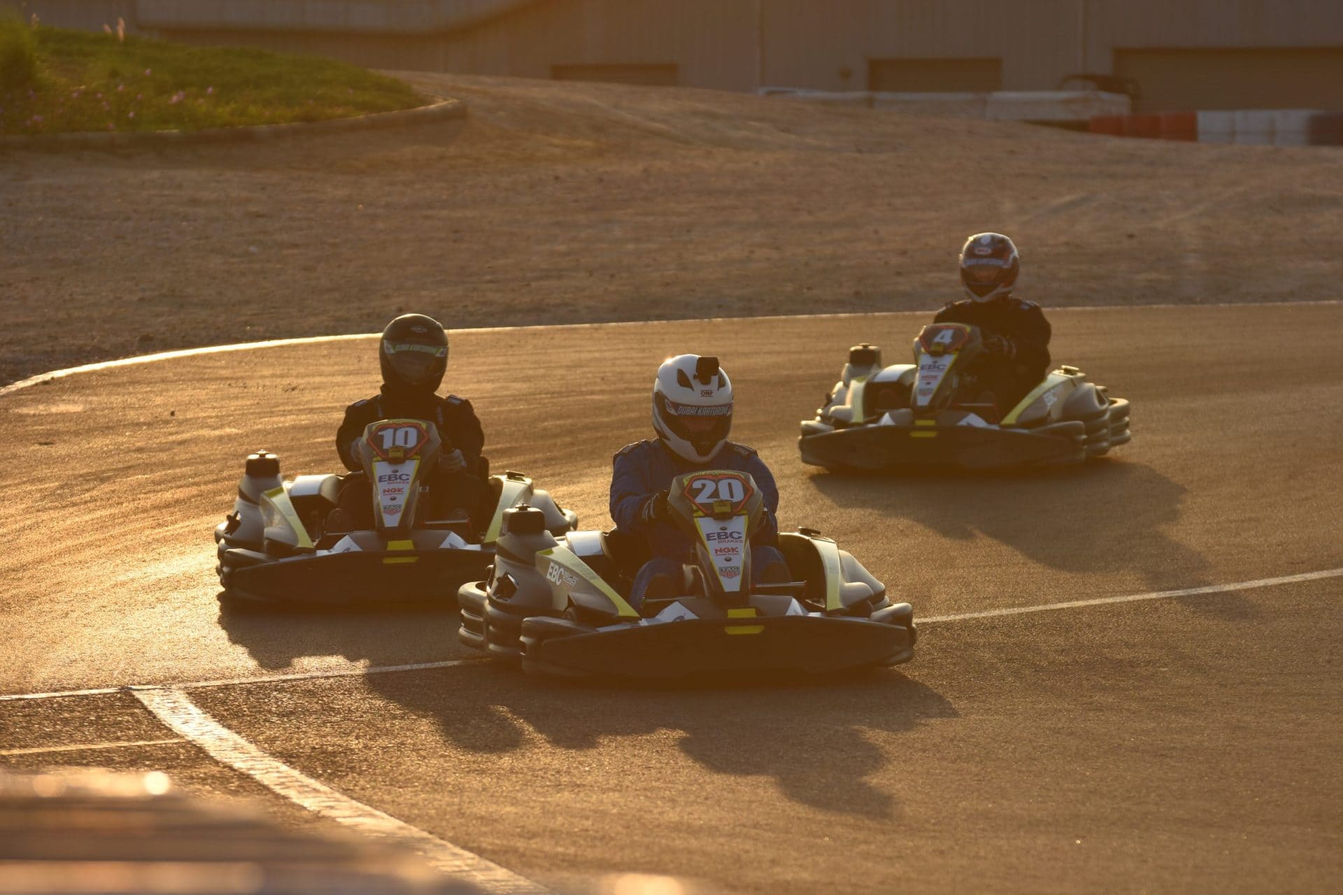 Three kart drivers with closed dark visors at Dubai Kartdrome in late light