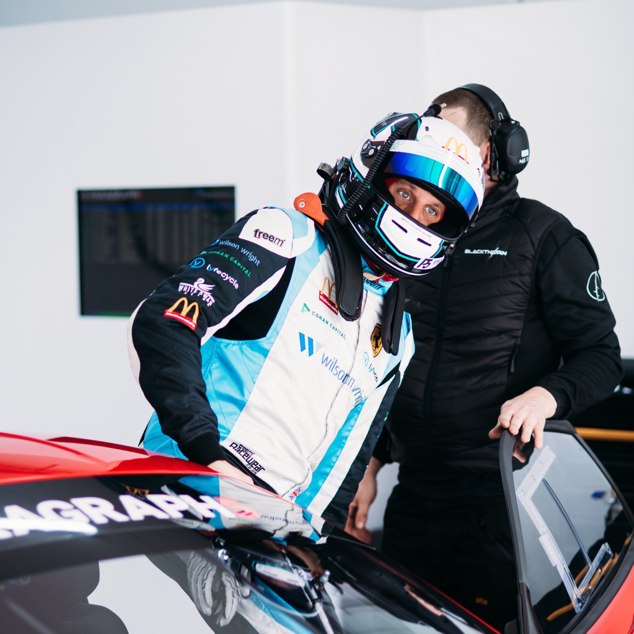 Jamie Unwin in racing equipment beside a race car, with a team member